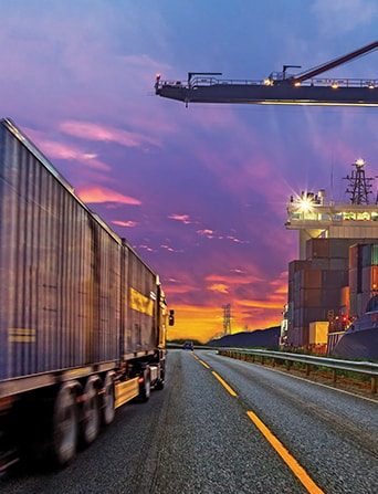 A lorry driving down a road beneath a purple sky.