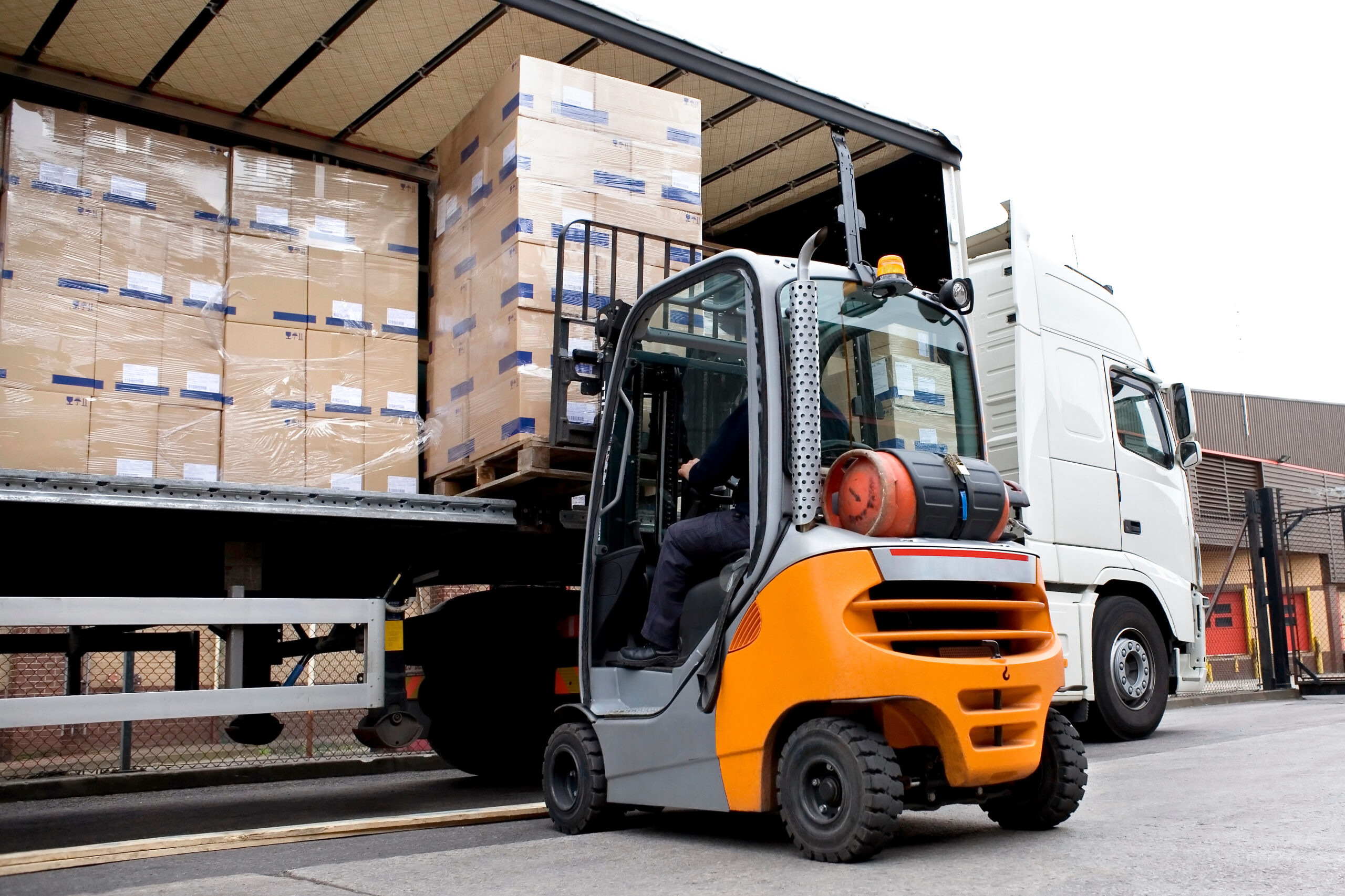 A forklift loads pallets stacked with cardboard boxes onto a heavy goods vehicle.