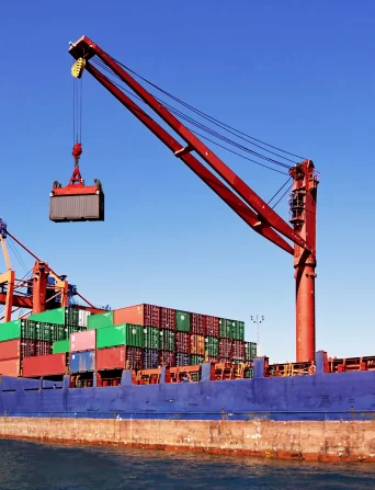 Red crane lowering shipping container onto large cargo ship.