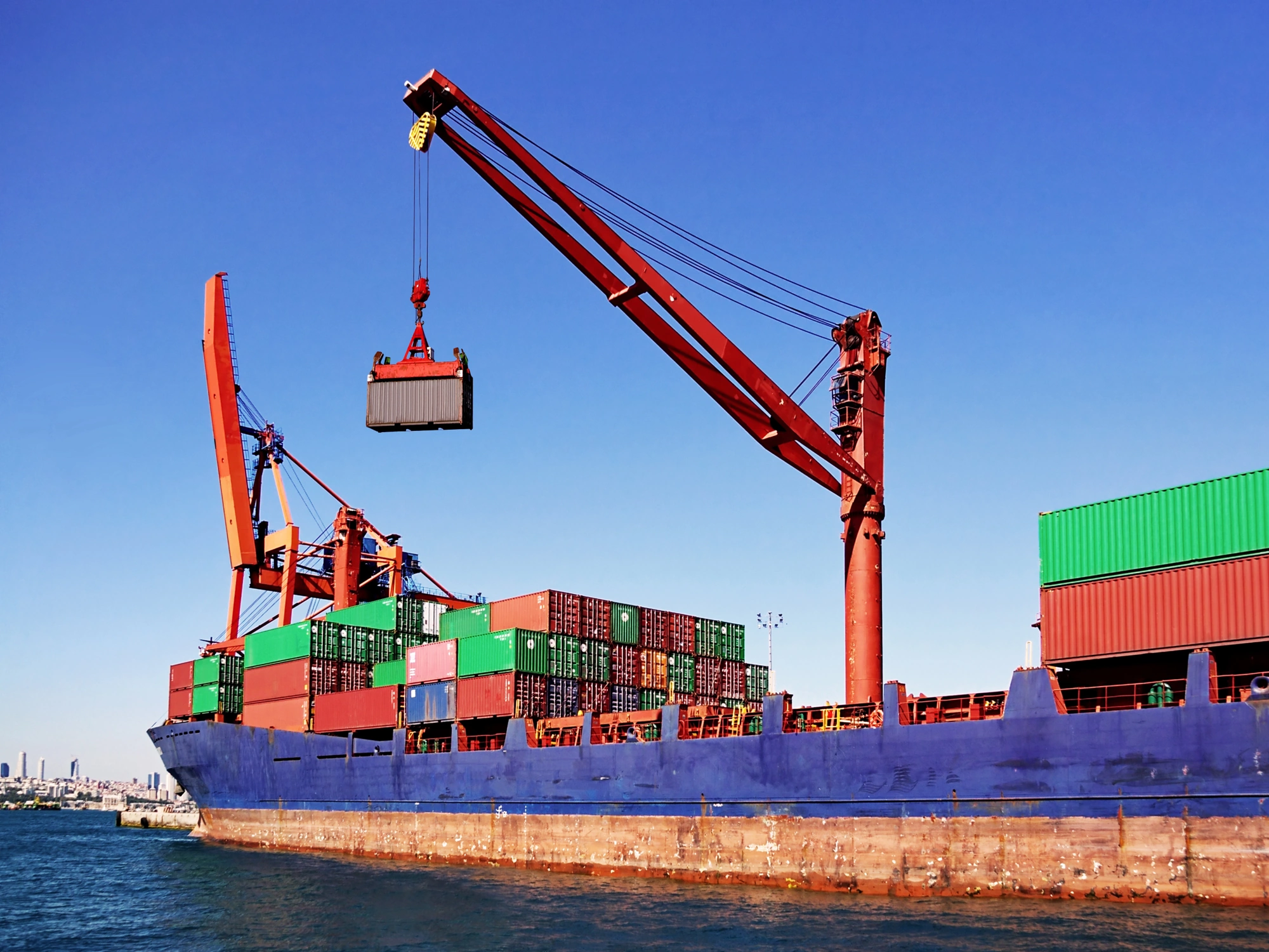 Red crane lowering shipping container onto large cargo ship.