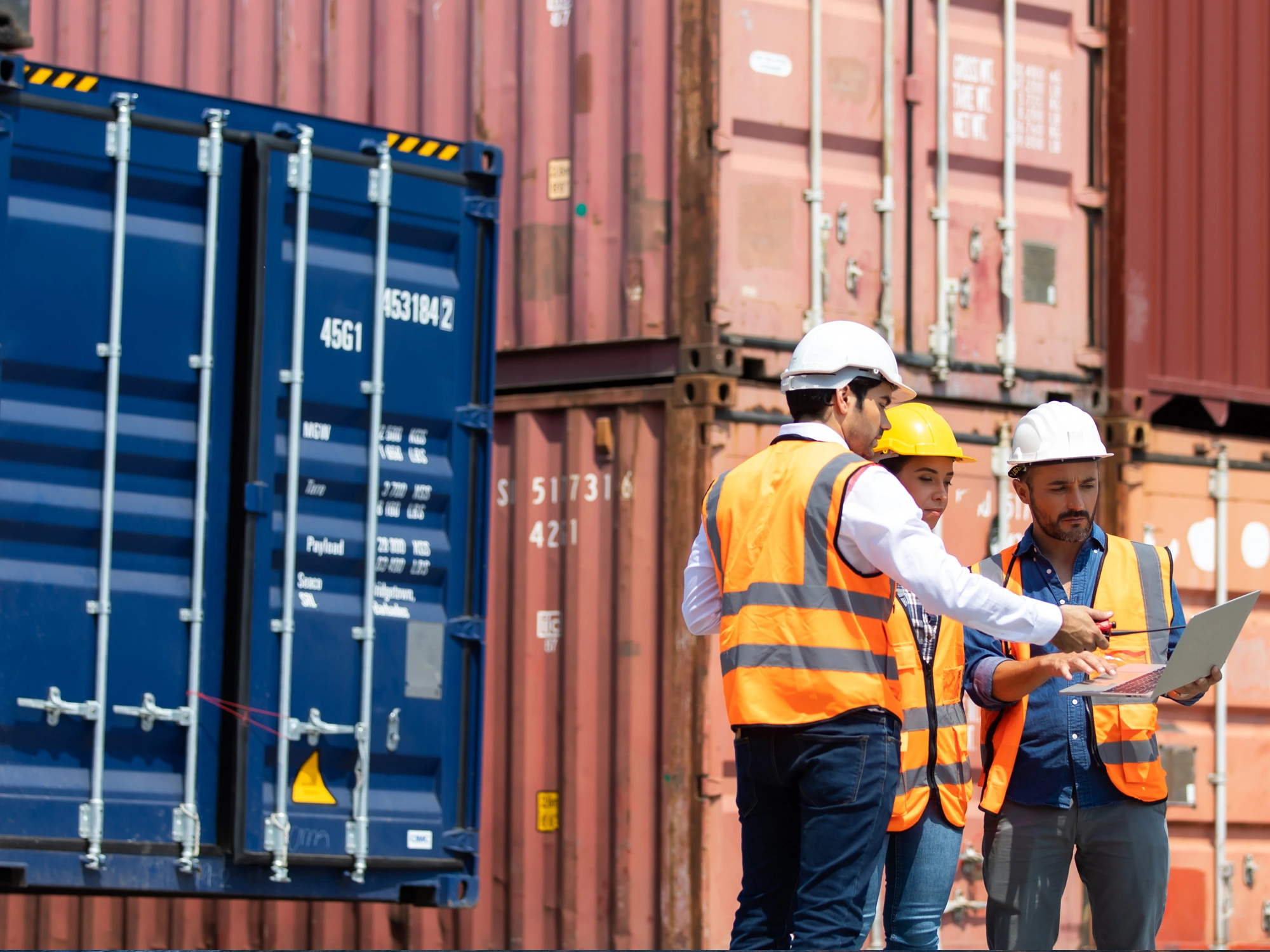 Three harbour workers in orange hi-vis vests talking to each other with containers in background.