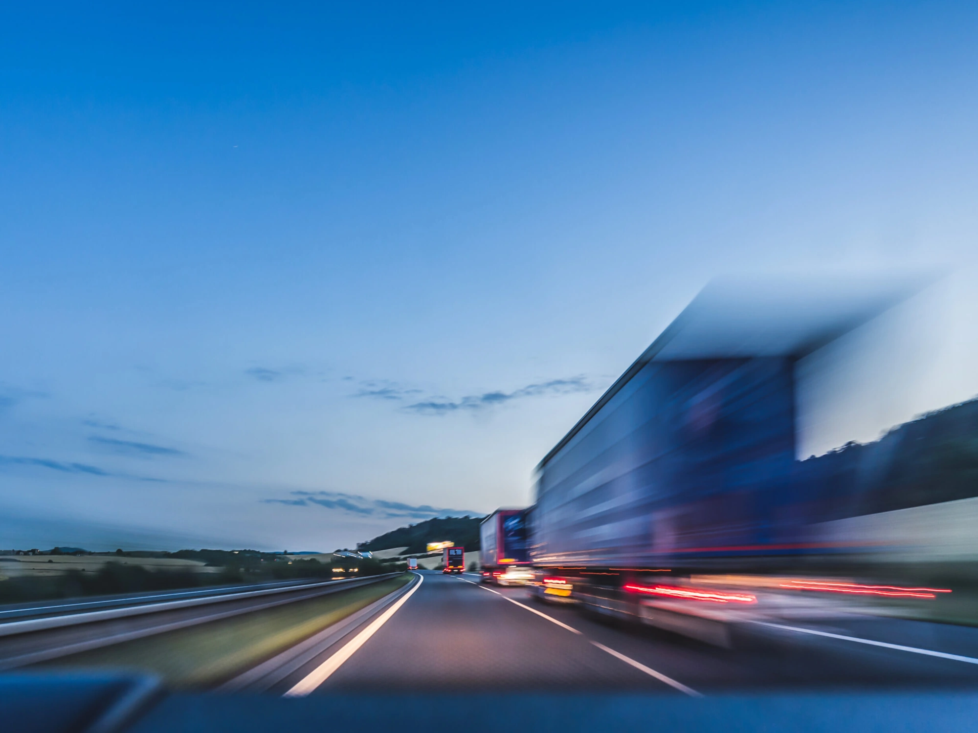 Blurred motion of a large truck overtaking on a motorway, with a clear blue sky and distant hills in the background, capturing the speed and movement of road transport. 