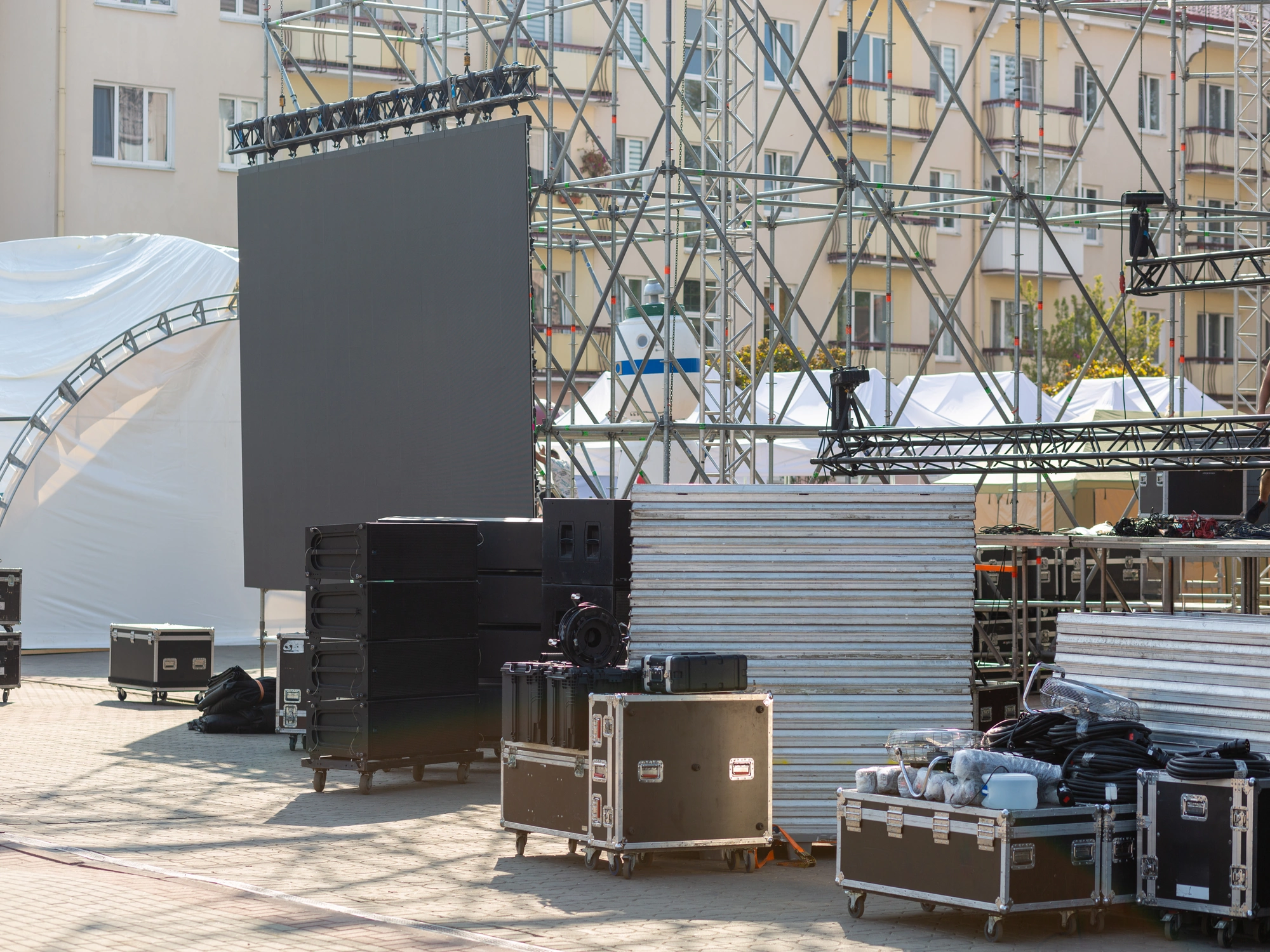 Outdoor event setup with large screen and black transport boxes.