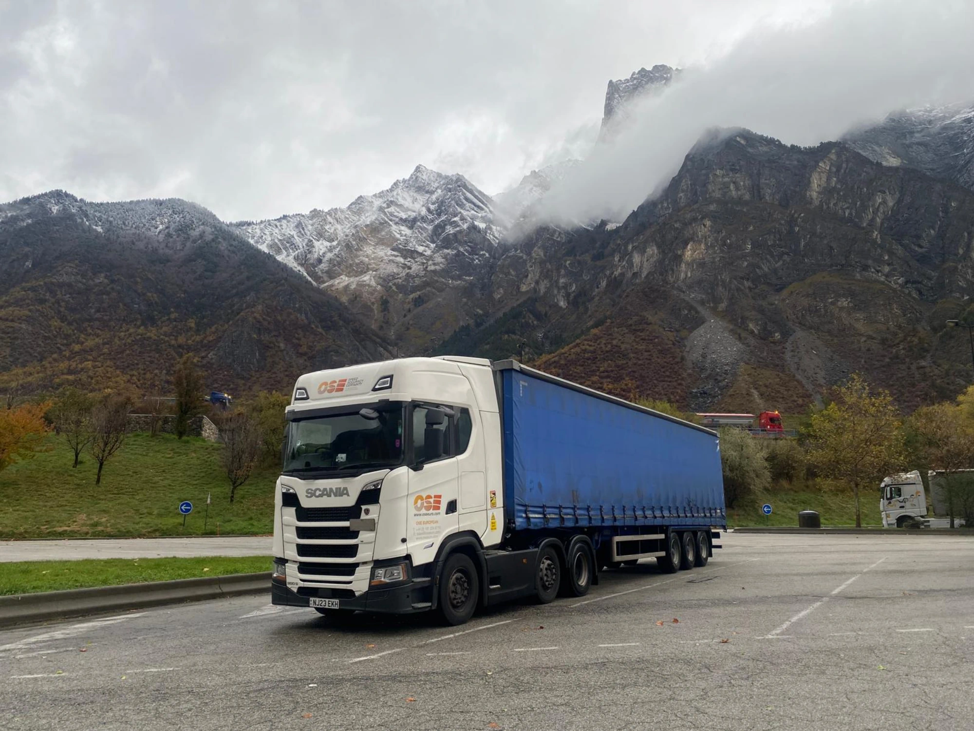 An OSE truck with a blue curtain-side trailer parked in a lot with snow-capped mountains in the background.