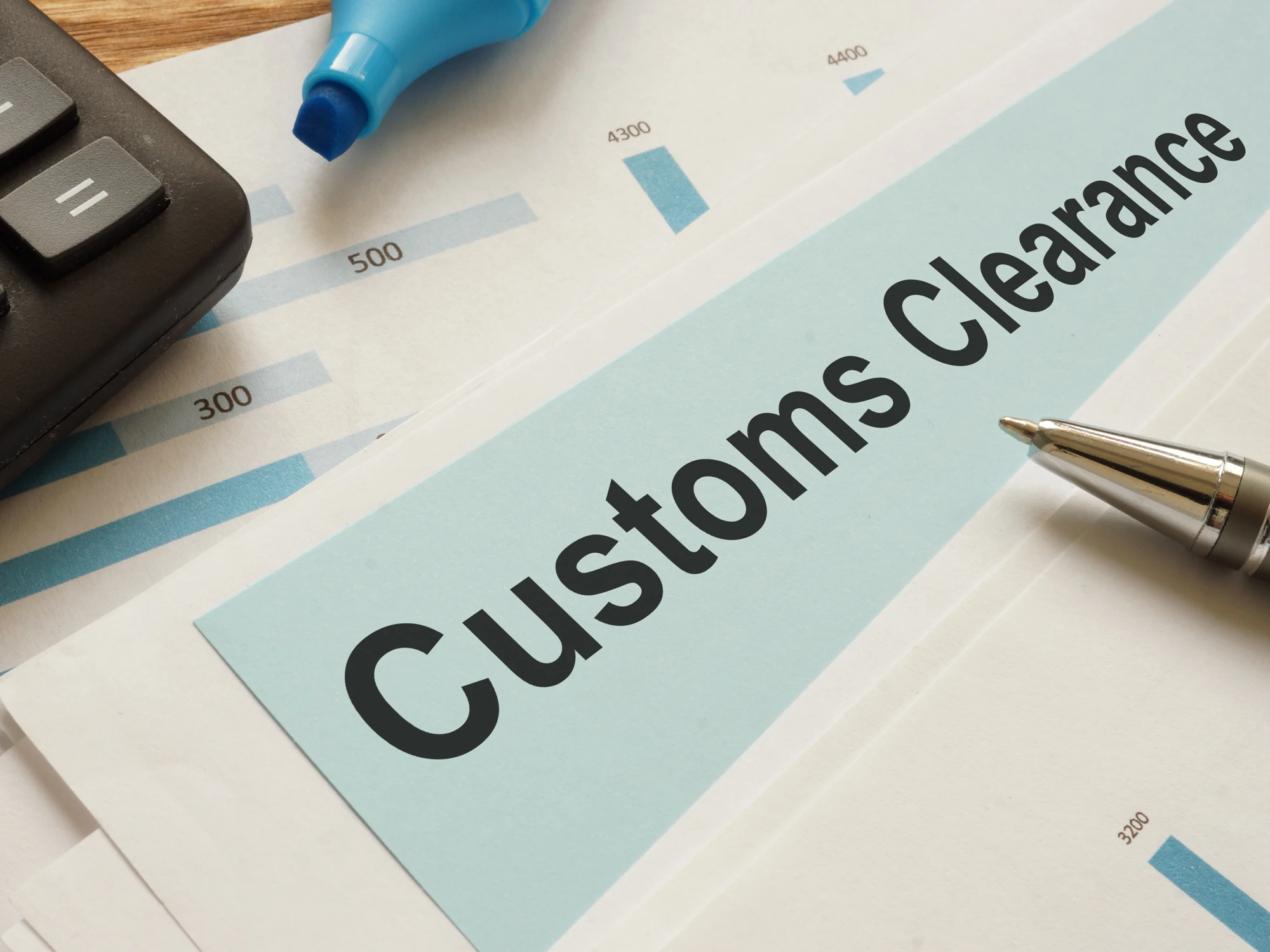 Customs clearance paperwork sits on a desk with a pen and calculator. 
