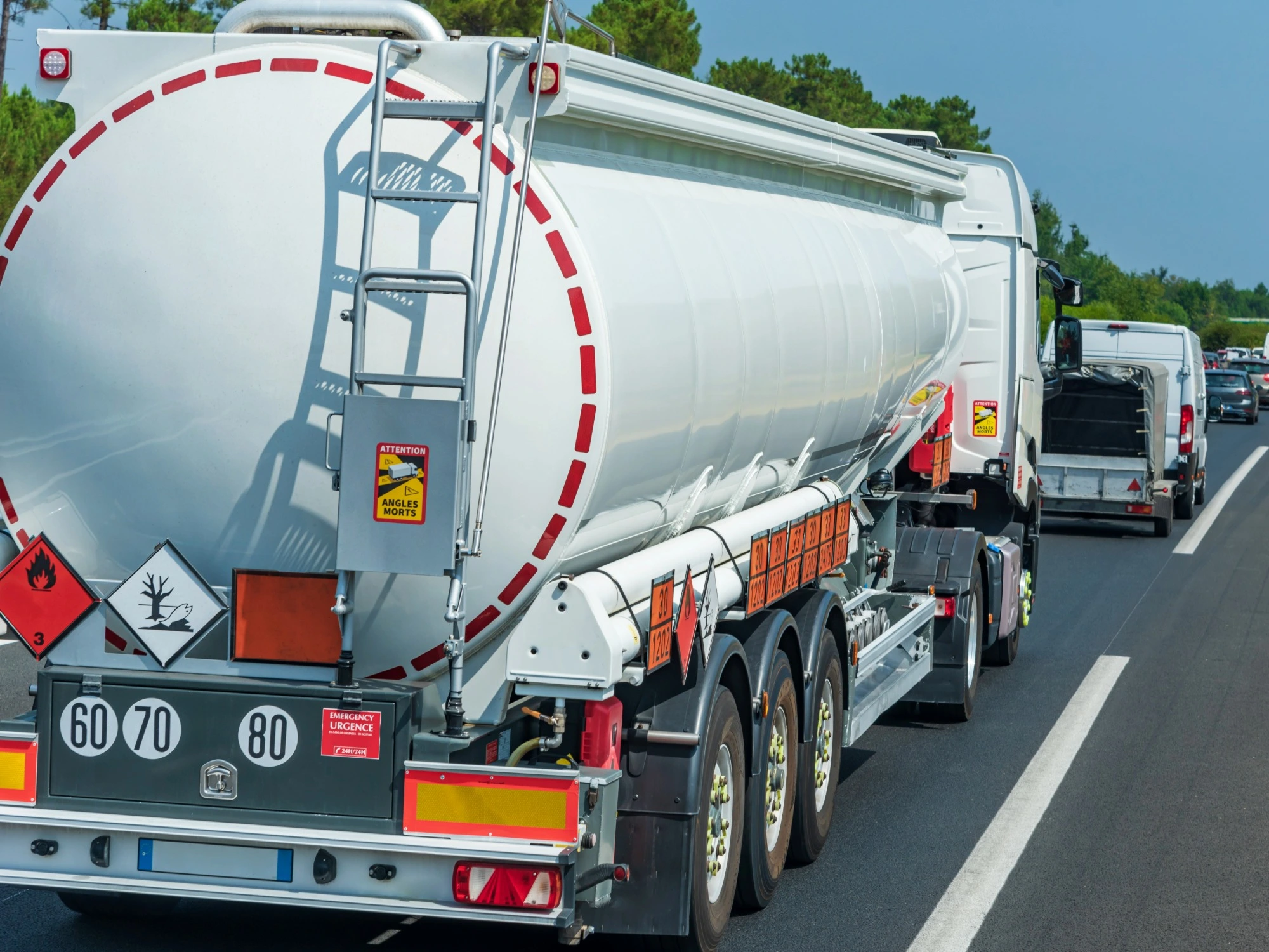 A large white lorry with warning signs on the back transporting hazardous goods along a motorway on a clear day.