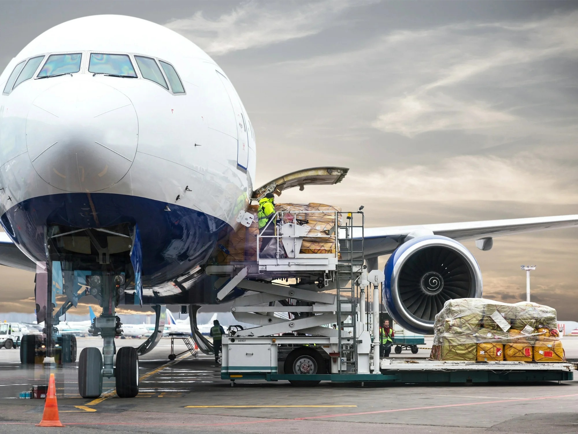 A front-facing shot of an airplane with a high-vis worker loading freight into the cargo hold on a cloudy day. 